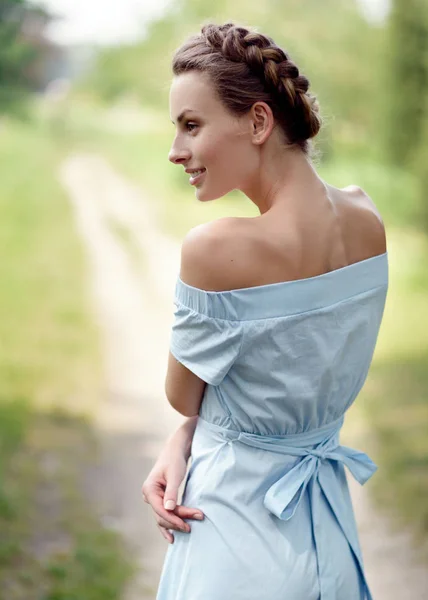 Szczupły młoda dziewczyna w niebieskiej sukience w parku w lecie jest z powrotem i pozowanie. Ładna fryzura. Pewien szczupły ciało — Zdjęcie stockowe