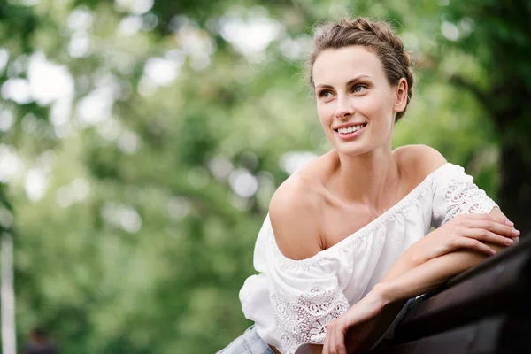 Retrato de una hermosa joven con pecas y una saludable sonrisa blanca como la nieve en un banco del parque en verano — Foto de Stock