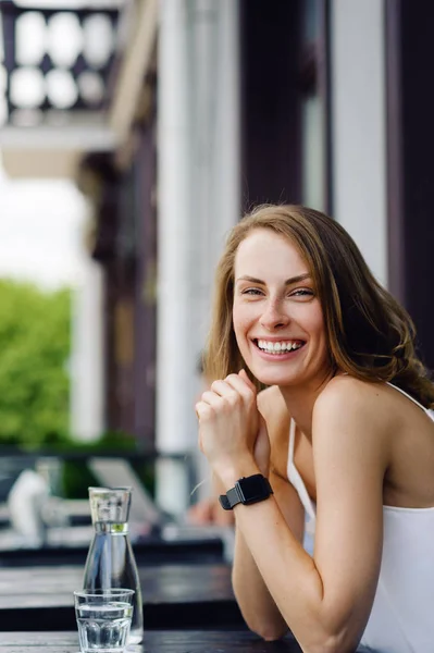 Piękna i młoda dziewczyna siedzi w letniej kawiarni i uśmiecha się. Na rękę Inteligentne zegarki — Zdjęcie stockowe
