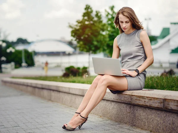 Mujer joven en la calle sentado y trabajando en su computadora portátil — Foto de Stock