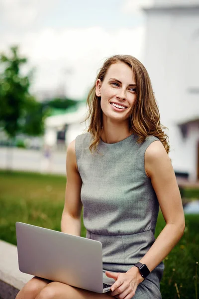 Mujer joven en la calle sentado y trabajando en su computadora portátil — Foto de Stock