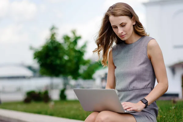 Mujer joven en la calle sentado y trabajando en su computadora portátil — Foto de Stock