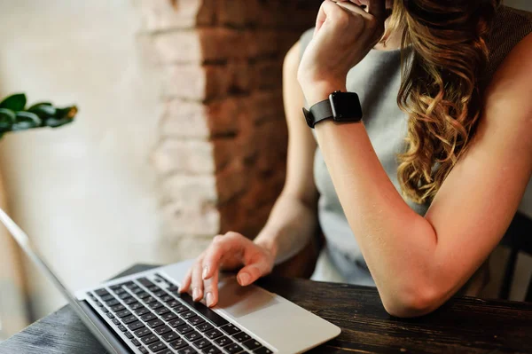 Manos de mujer usando smartwatch en el teclado de su computadora portátil. Mujer trabajando en el ordenador portátil en un café . — Foto de Stock