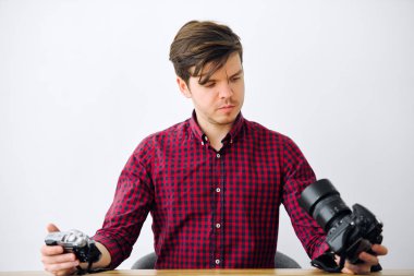 Ofiste genç adam bir masada oturur ve dijital kameralar görünüyor. Tablo aynasızlar ve ayna kamera