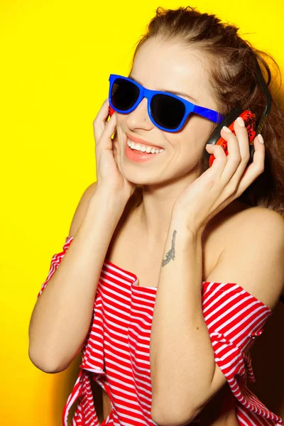 아름 다운 젊은 섹시 한 여자 dj는 블루 선글라스와 레드 스트라이프 티셔츠 웃음과 재미와 노란 배경에 빨간 헤드폰에서 음악을 듣고 — 스톡 사진