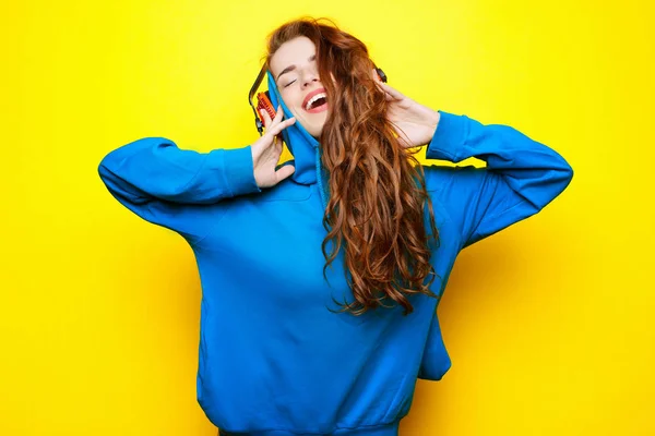 年轻漂亮性感的女孩 Dj 在蓝色夹克在黄色的背景和有乐趣的红色耳机听音乐 — 图库照片