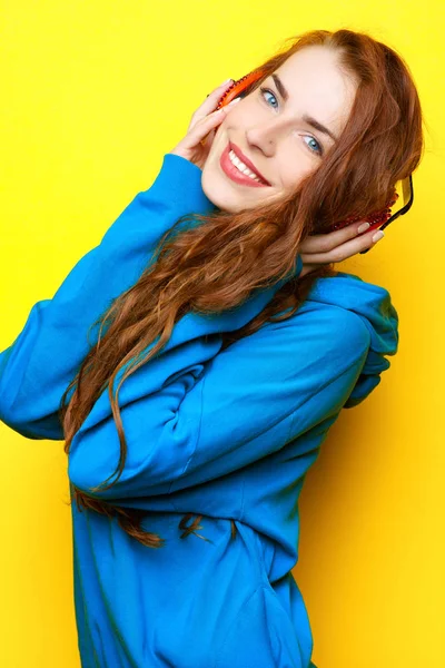 Hermosa joven sexy chica DJ en una chaqueta azul escuchando música en auriculares rojos sobre un fondo amarillo y divertirse — Foto de Stock