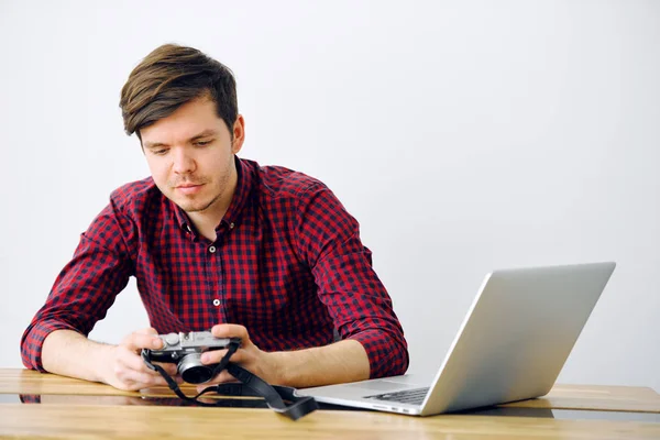 Young and successful man uses Mirrorless camera and sits at a table with a laptop in the office