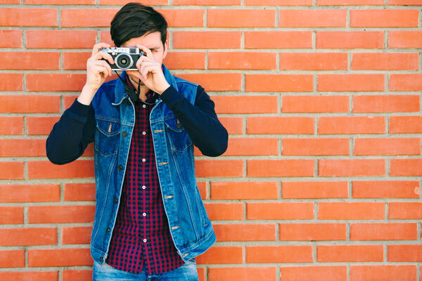 Young and handsome guy stands by a brick wall and takes pictures on a mirrorless camera