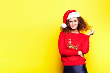 Geyik eğlence gülümseyen genç güzel santa Noel şapka içinde kırmızı kadın kazak gülüyor sevinir stüdyoda sarı arka plan dokunuşlar dokunur. İsa'nın tatil kavramı