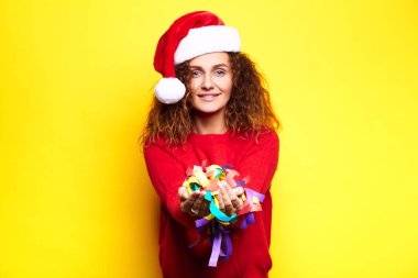 Bir geyik ile kırmızı bir kazak giyen Noel şapkalı genç güzel kız stüdyoda sarı bir arka plan üzerinde dokunur endişeli gülümseyen eğlenceli mutlu gülüyor sahip sevinir konfeti atar. Kavramı 
