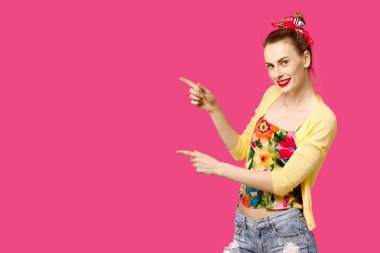 Pembe bir arka plan üzerinde sarı kazaklı genç güzel kız ok gösterir. Renk obsesyon kavramı. Minimalist tarzı, şık moda