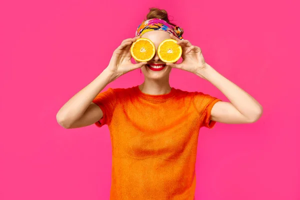 粉红色背景的年轻女子在她的手里拿着一个切橙, 笑了起来。色彩痴迷的概念。简约风格。时尚时尚 — 图库照片