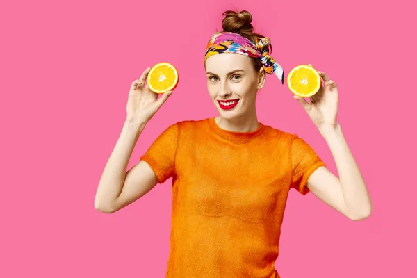 Jovem mulher em um fundo rosa segura uma laranja de corte em suas mãos e ri. Conceito de obsessão a cores. Estilo minimalista. Elegante moda — Fotografia de Stock