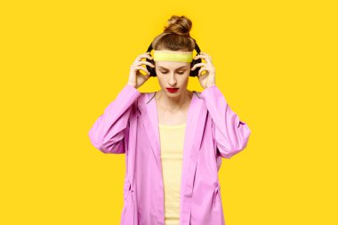 Sarı bir arka plan ve pembe bir ceket genç kadın müzik solucan kablosuz kulaklık sarılmak. Renk obsesyon kavramı. Minimalist tarzı. Şık Trendy