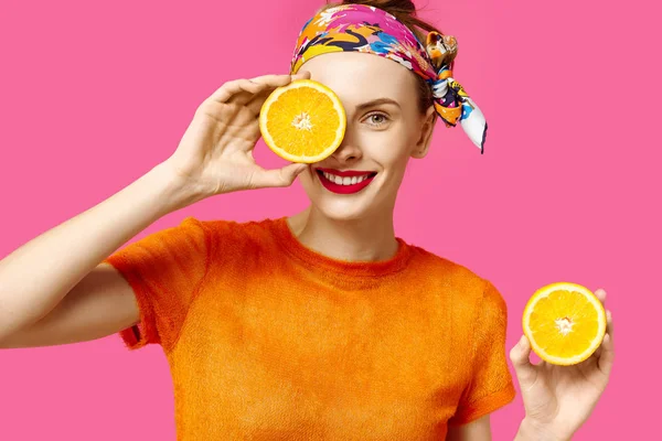 Молодая женщина на розовом фоне держит порезанный апельсин в руках и смеется. Концепция цветовой одержимости. Минималистический стиль. Стильный тренд — стоковое фото