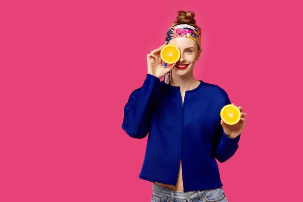 Jovem mulher em um fundo rosa segura uma laranja de corte em suas mãos e ri. Conceito de obsessão a cores. Estilo minimalista. Elegante moda — Fotografia de Stock