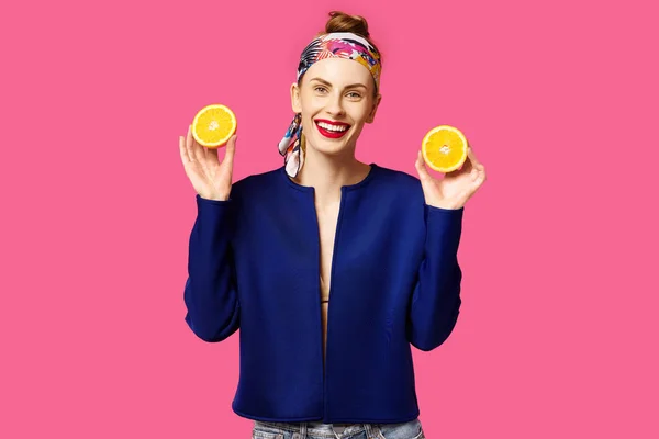 Mujer joven sobre un fondo rosa sostiene un corte naranja en sus manos y se ríe. Concepto de obsesión por el color. Estilo minimalista. Moda con estilo — Foto de Stock