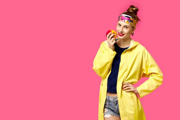 Jovem mulher em um fundo rosa e um casaco amarelo segura uma maçã em suas mãos. Conceito de nutrição saudável e esportes. Conceito de obsessão a cores. Estilo minimalista. Elegante moda — Fotografia de Stock