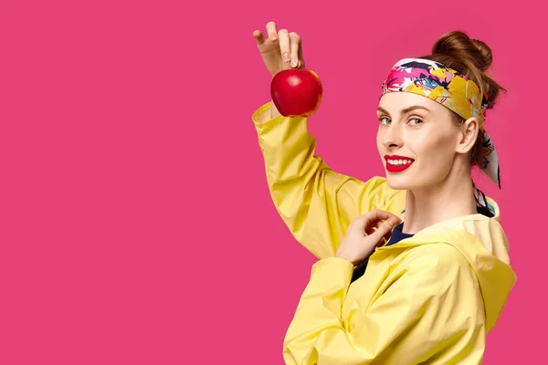 一个粉红色的背景和黄色的大衣的年轻女子在她手中持有一个苹果。健康营养和体育的概念。色彩痴迷的概念。简约风格。时尚时尚 — 图库照片