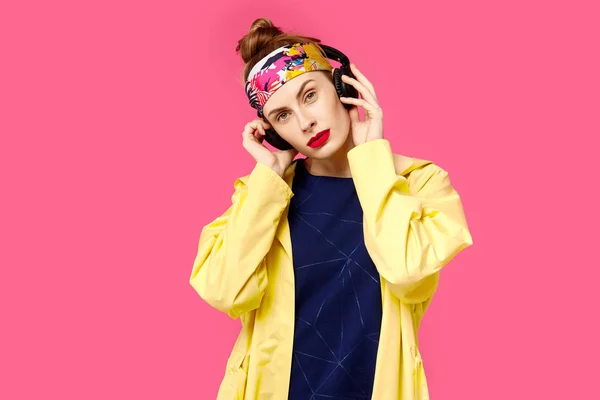 Junge schöne Frau auf rosa Hintergrund und gelbem Mantel, die über drahtlose Kopfhörer Musik hört. Konzept der gesunden Ernährung und Sport. Farbbesessenheit. Minimalistischer Stil. st — Stockfoto