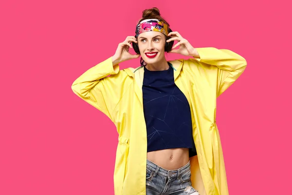 Giovane bella donna su uno sfondo rosa e un cappotto giallo ascoltare musica attraverso cuffie wireless. Concetto di alimentazione sana e sport. Il concetto di ossessione per il colore. Stile minimalista. St. — Foto Stock