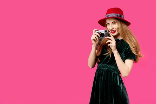 Jovem mulher bonita em um fundo rosa em um vestido verde e chapéu tem uma câmera de raridade em suas mãos e sorrisos. Conceito de nutrição saudável e esportes. Conceito de obsessão a cores. Poeira minimalista — Fotografia de Stock