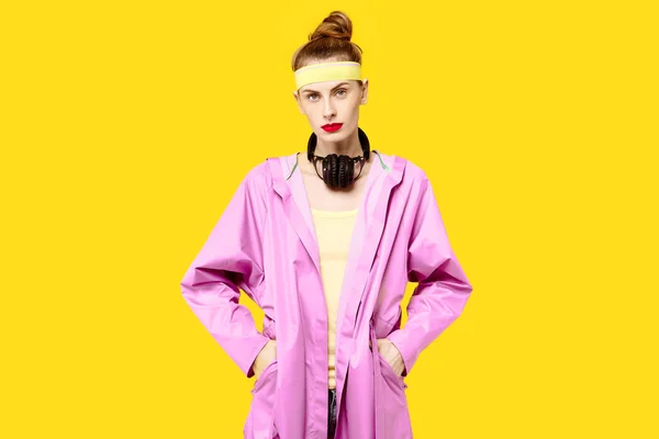Mujer joven sobre un fondo amarillo y un abrigo rosa abraza los auriculares inalámbricos gusano de la música. Concepto de obsesión por el color. Estilo minimalista. Moda con estilo — Foto de Stock