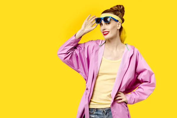 在黄色背景和粉红色外套和太阳镜的年轻妇女。色彩痴迷的概念。简约风格。时尚时尚 — 图库照片