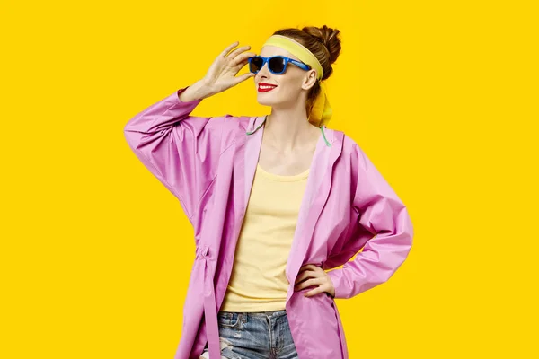 Giovane donna su sfondo giallo e cappotto rosa e occhiali da sole. Il concetto di ossessione per il colore. Stile minimalista. Trendy alla moda — Foto Stock