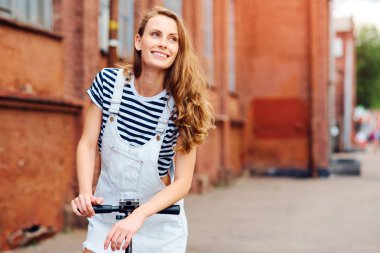 Genç güzel kız scooter üzerinde cadde boyunca yaz aylarında bir scooter sürme. Sağlıklı bir yaşam tarzı kavramı