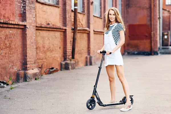 Giovane bella ragazza sta cavalcando uno scooter in estate lungo la strada sullo scooter. Il concetto di uno stile di vita sano — Foto Stock