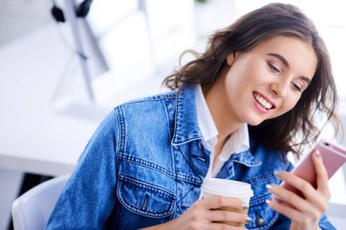 Ofisteki genç bayan kahve içiyor ve telefonda geziniyor. Çatı katındaki hippi kız