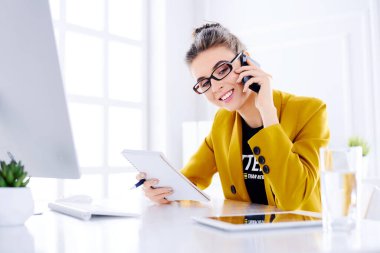 Genç iş kadını ofisinde telefonla konuşuyor ve defterini tutuyor.
