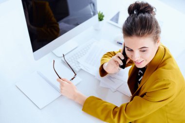 Masaüstü bilgisayarlı iş kadını ofisinden telefonla konuşuyor.