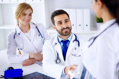 Genç gülümseyen Arap doktor hastanede bir hemşireyle tokalaşıyor. Ofiste ırklar arası genç doktorlar var.