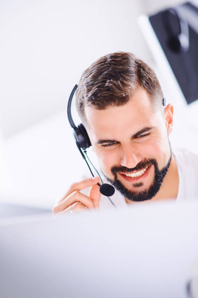 Young smiling customer support operator with hands-free headset working in the office. Concept