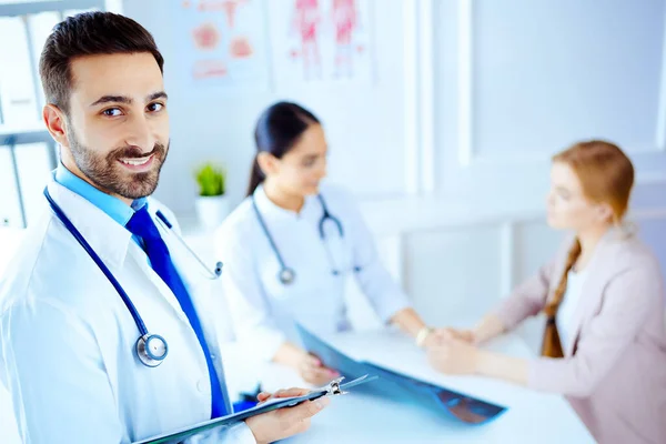 Arab doctor in the hospital with tablet and stethoscope, nurse working with patient on the background