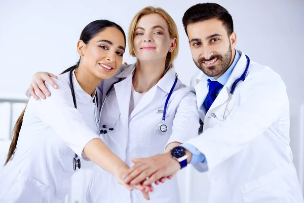病院の3人の若い医者が手を合わせて笑っている 多人種的概念 — ストック写真