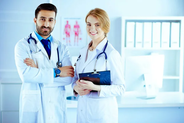 Two mixed races doctors all standing together in a consultancy room and holding patient notes