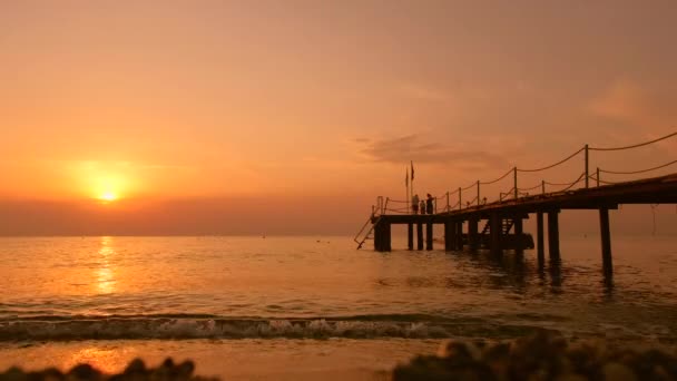 Kemer, Turcja - 10.14.2019 Zachód słońca nad plażą nad morzem. Ludzie chodzą po molo. Sylwetki ludzkie — Wideo stockowe