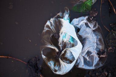 Thrown away plastic bags floating in black dirty water clipart