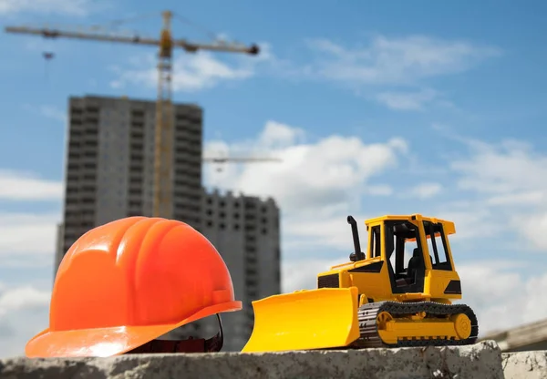 Строительный шлем и игрушечный бульдозер на строительной площадке — стоковое фото