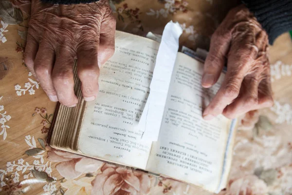 Old woman hands on the open prayer book.