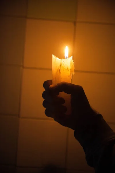 Mão segurando a vela contra a parede de azulejos — Fotografia de Stock