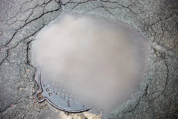 La pozzanghera sul tombino in superficie asfaltata — Foto Stock