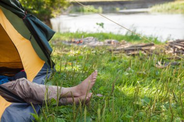 Kampçı nehrin yanındaki çadırda yatıyordu. Kampçı bacakları çadırdan dışarı sarkmış..