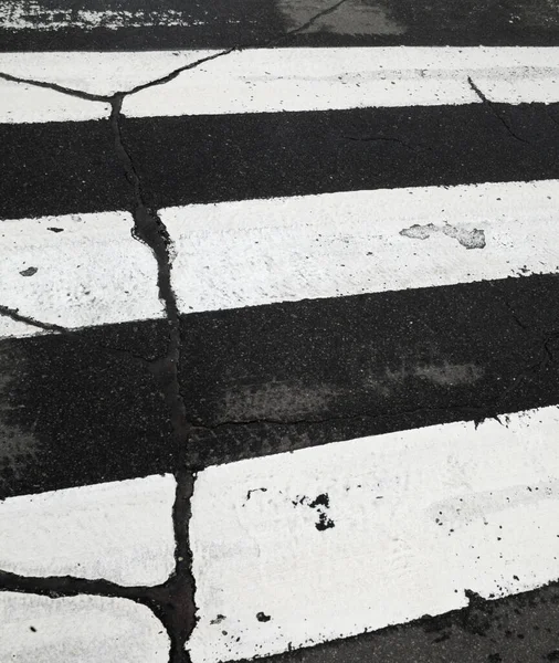 White zebra crossing lines on the road. Pedestrian crossing. Cracked surface. Potholes on the road.