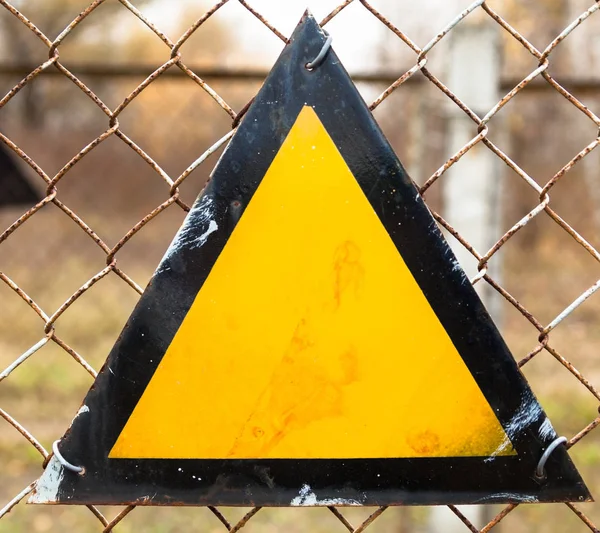 Triangle warning sign on the metal mesh fence. Basic warning sign triangle with a black border and amber background.