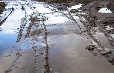 Toprak yolda çamur ve su birikintileri.